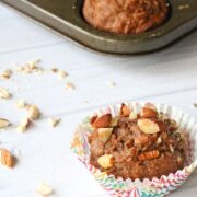 Healthy, sugar free carrot muffin topped with chopped almonds in a colored cupcake liner with more muffins in a muffin tray behind it.