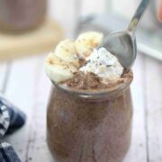 Chocolate chia pudding in a jar with whole30 whipped cream and bananas on top and a spoon going into the jar.