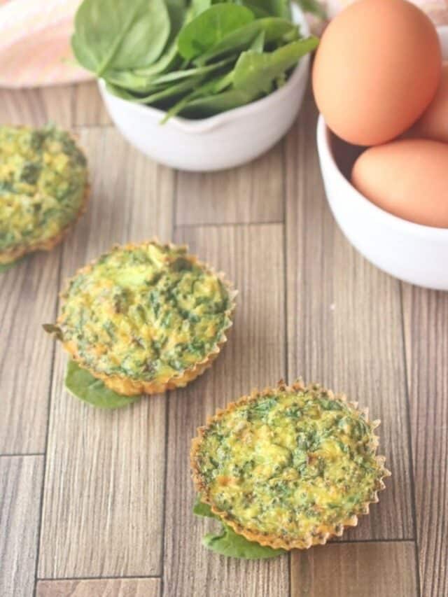 dairy-free egg muffins in a line seated on spinach with eggs and spinach in white bowls