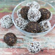 Chocolate coconut energy balls with dates in a glass bowl with three energy balls beside the bowl and coconut around it.