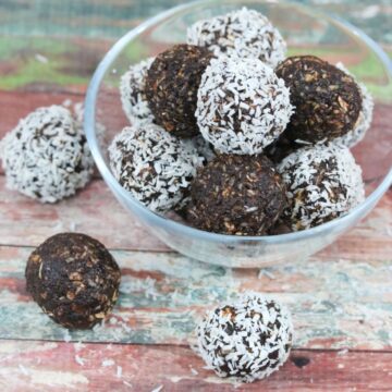 Chocolate coconut energy balls with dates in a glass bowl with three energy balls beside the bowl and coconut around it.