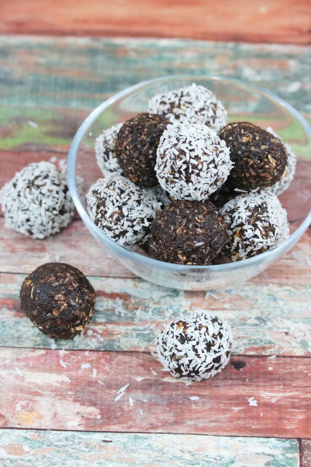 Chocolate coconut energy balls with dates in a glass bowl with three energy balls beside the bowl and coconut around it.