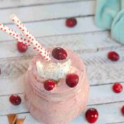 Apple cranberry smoothie i a mason jar with whole30 whipped cream and cranberries on top with frozen cranberries around the jar.