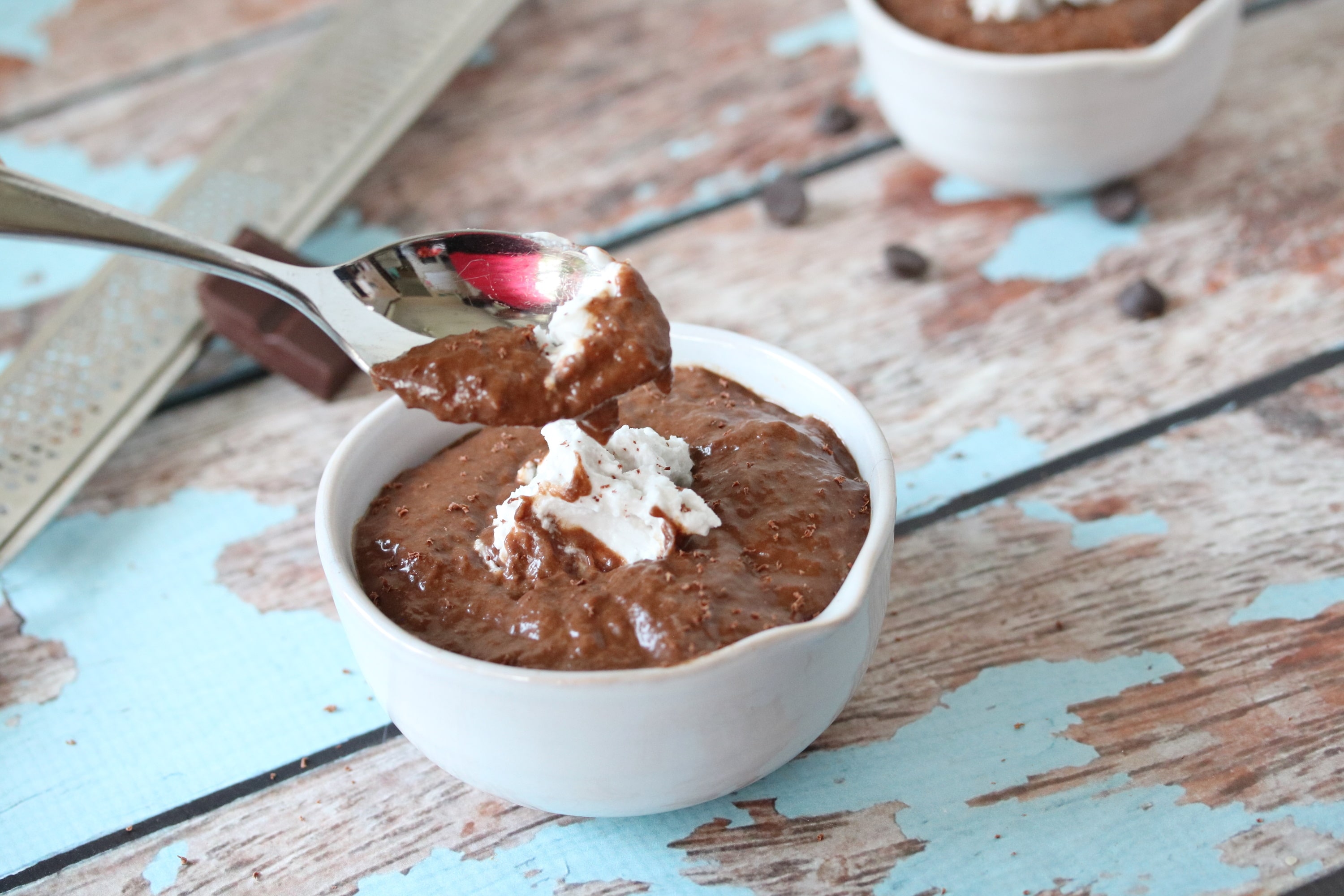 dairy-free chocolate pudding in a white ramekin with coconut whip cream on top and a spoon pulling out of the pudding