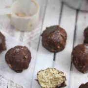 Multiple chocolate protein coconut balls lined up and one with a bite out of it, with protein powder off to the side.