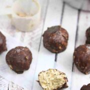 Multiple chocolate protein coconut balls lined up and one with a bite out of it, with protein powder off to the side.