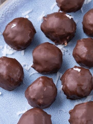 Chocolate coated coconut protein balls on a blue plate.