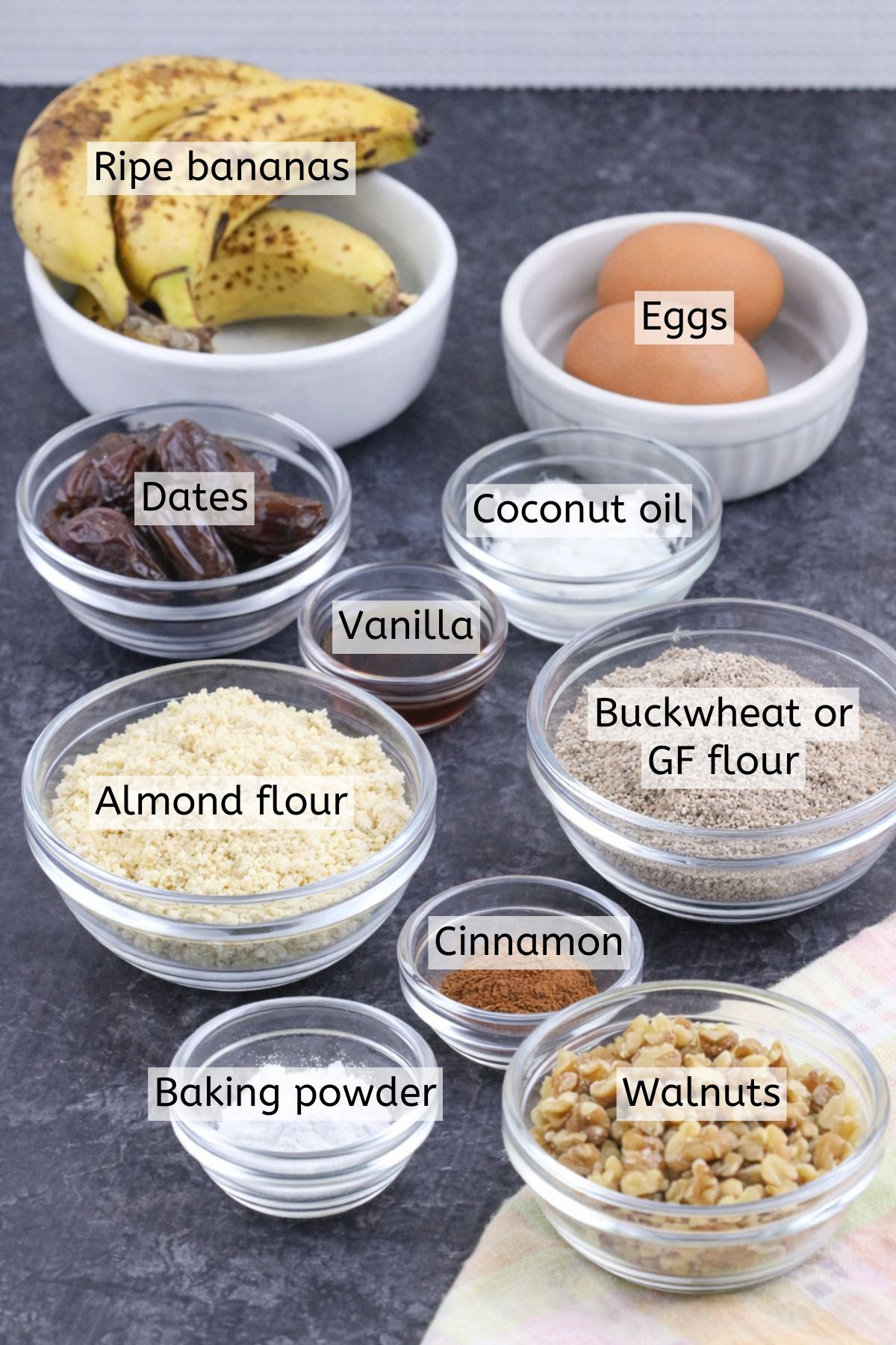 Bananas, flours, cinnamon, eggs, and oil in glass bowls with text labels over top.