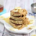 Peanut butter pancakes topped with bananas and peanut butter on a white plate.