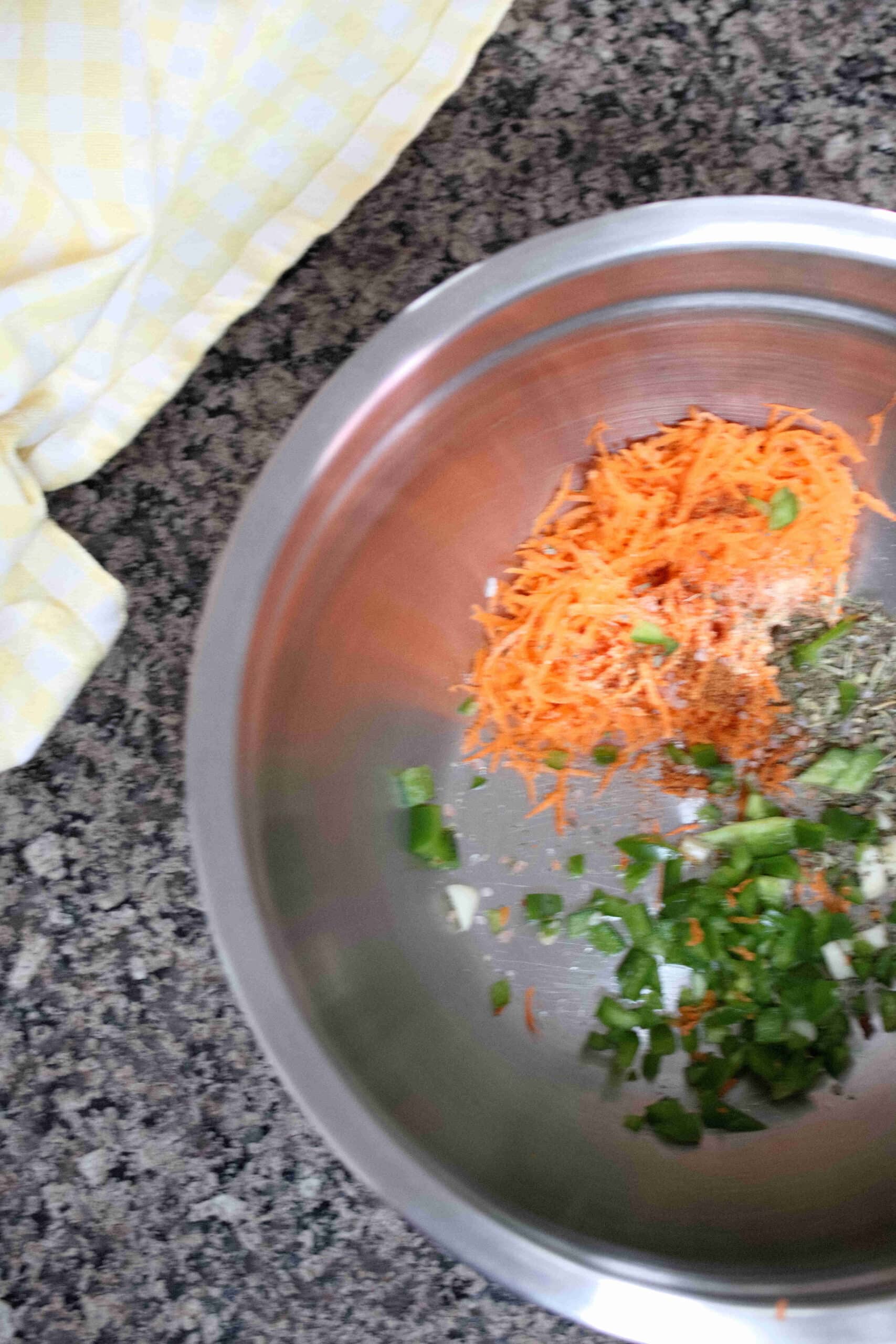 Steel bowl with grated carrots, garlic, and jalapenos in it.