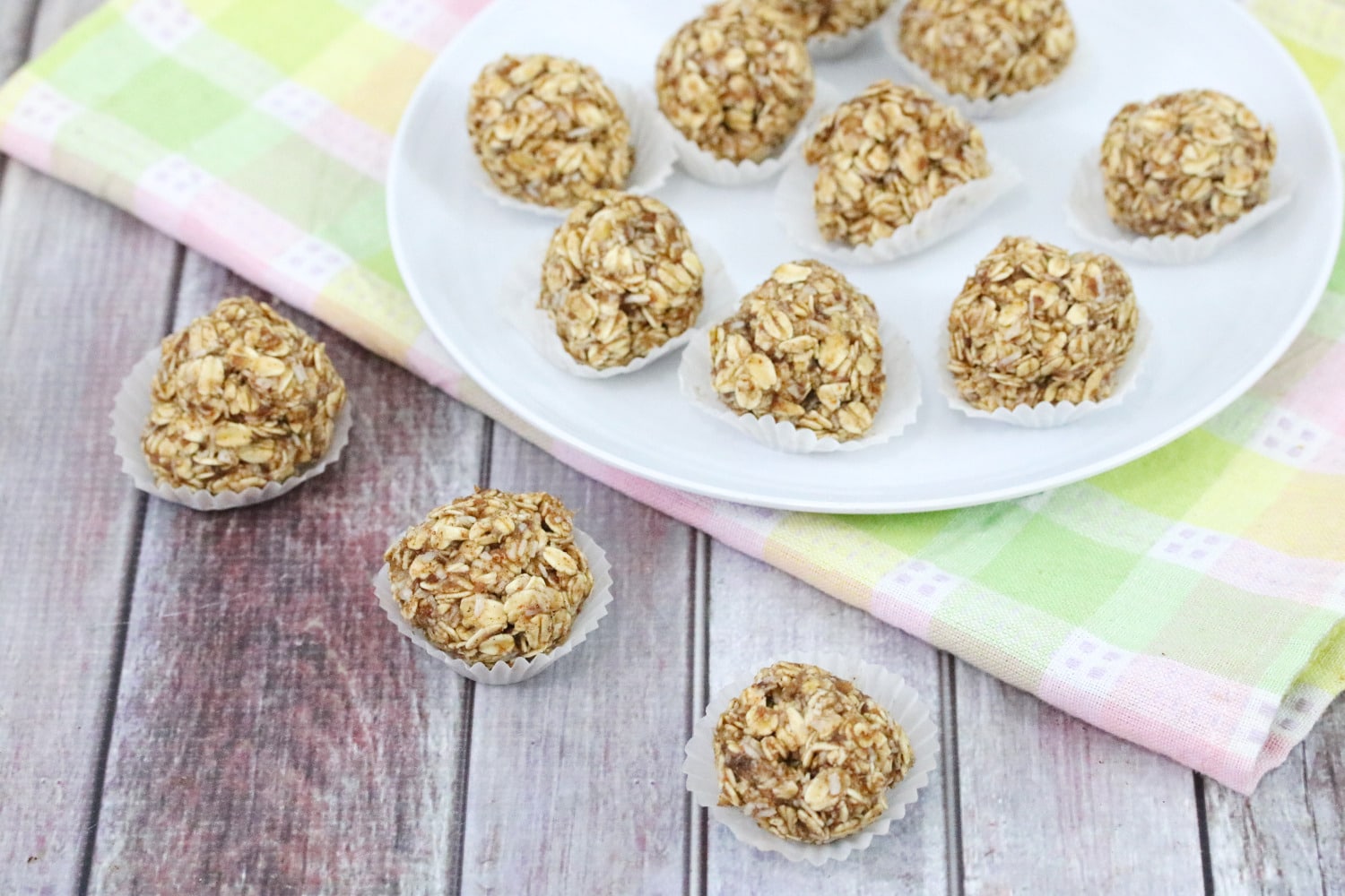 Multiple banana protein balls in mini muffin tins lined up with more protein balls on a white plate and colored linen behind them.
