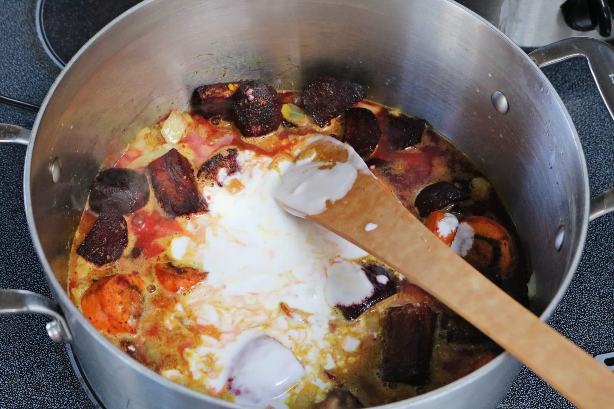 In process image for beet soup: coocnut milk, beets, onions and broth cooking in a large pot