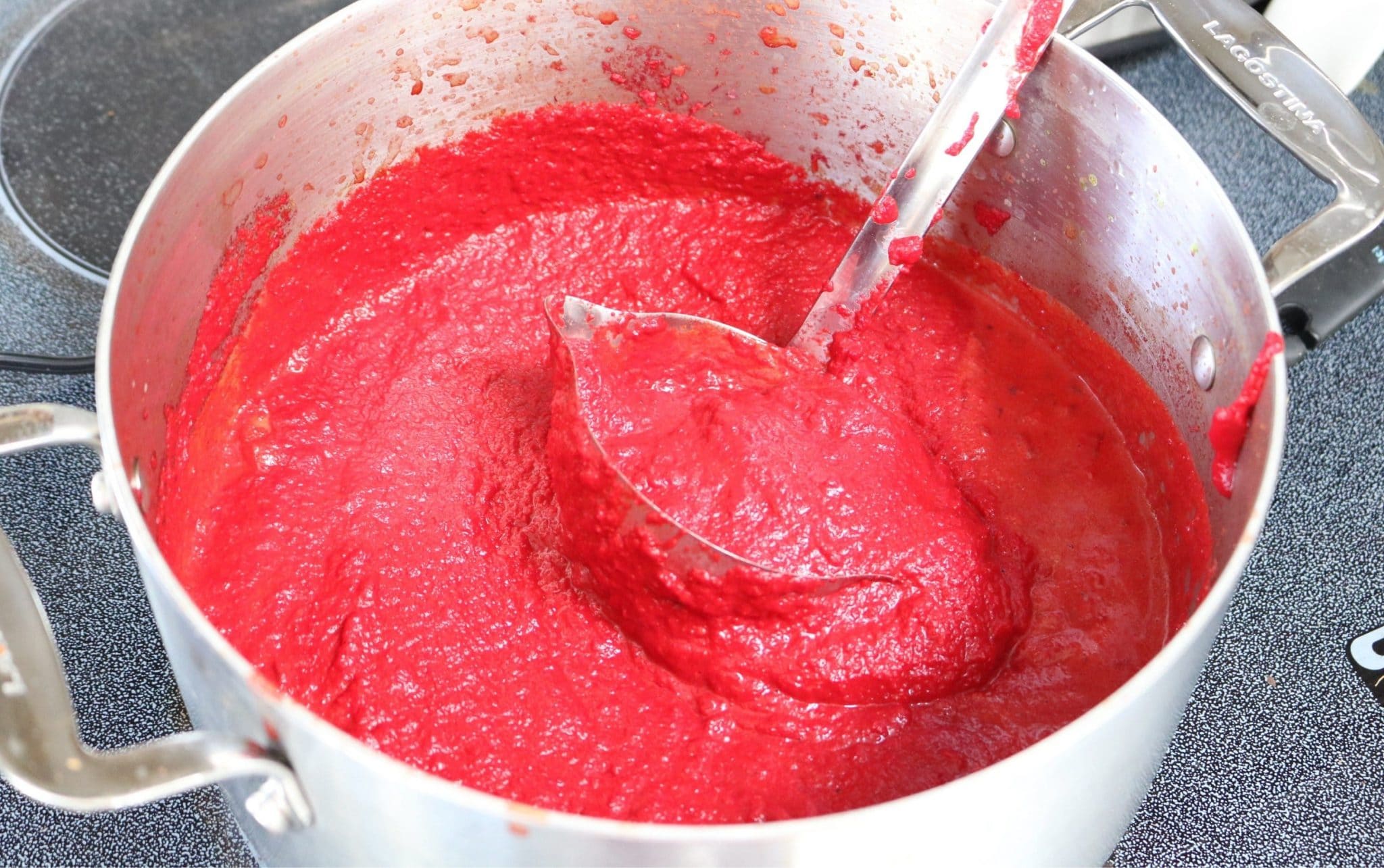 In process image for beet soup: large pot of beet soup blended with ladle scooping