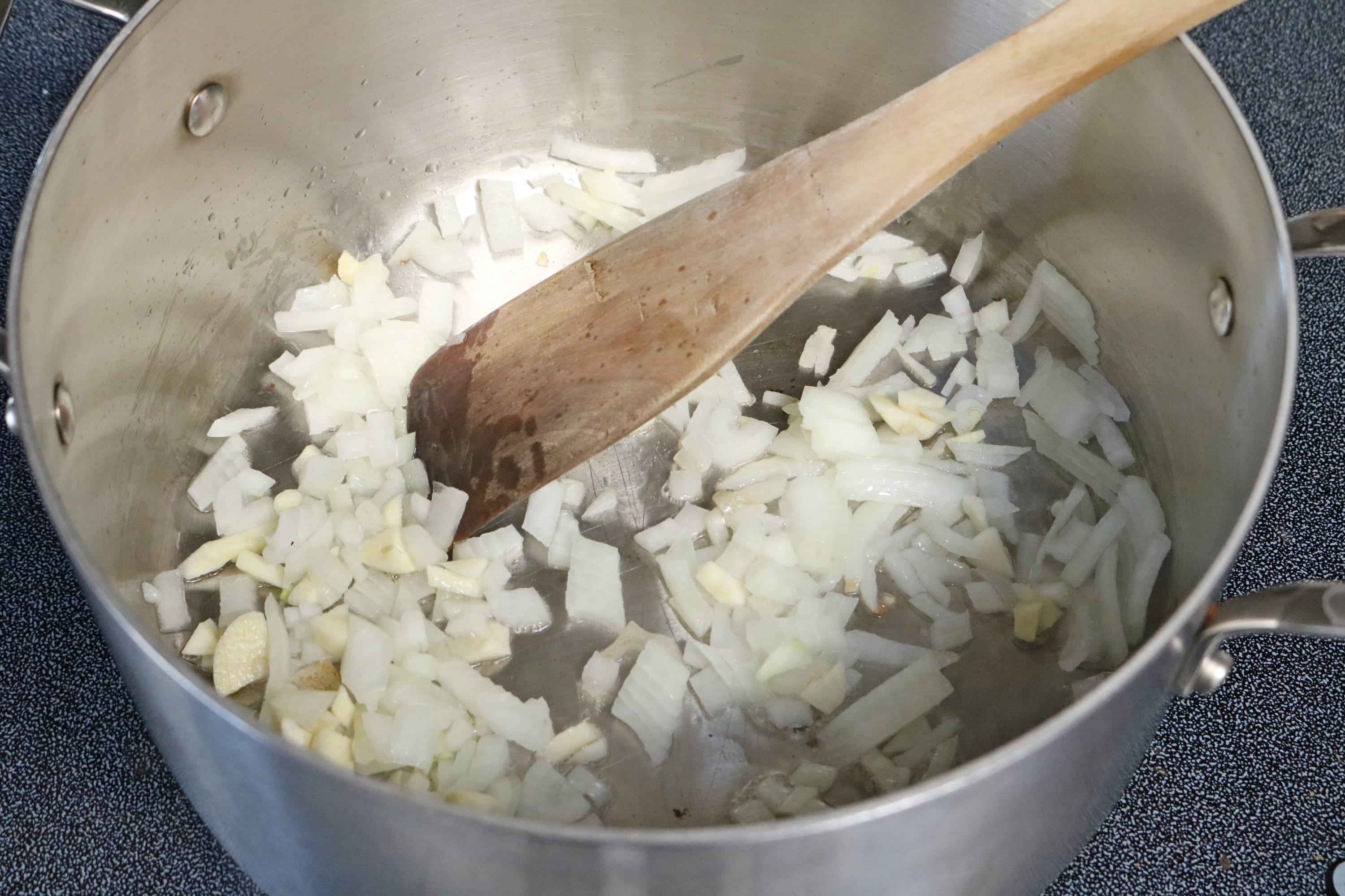 Onions and garlic being sauteed in a pot with a wooden spoon