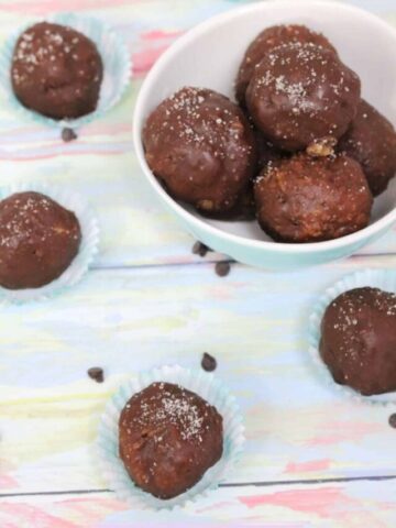 Chocolate covered cake balls on mini muffin cups with chocolate chips around them.