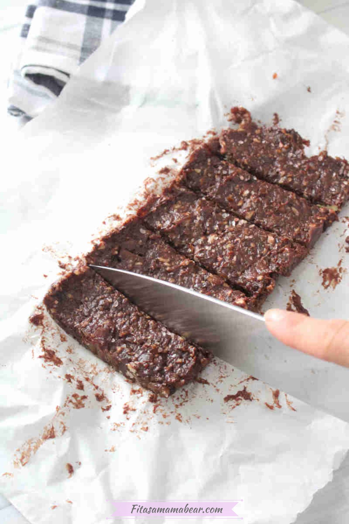 Chocolate date protein bars on parchment paper being sliced.