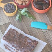 Three chocolate energy bars stacked with parchment paper between them and ingredients in measuring cups behind them.