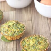 Dairy-free egg muffins in a line seated on spinach with eggs and spinach in white bowls.