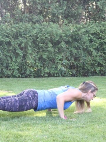 Woman in blue shirt and dark pants performing a push up outside