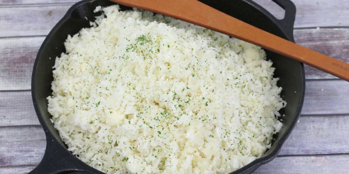 Cauliflower rice in a skillet with a wooden spoon over it.