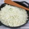 Black pan with cauliflower rice in it and a wooden spoon ontop.