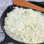 Black pan with cauliflower rice in it and a wooden spoon ontop.