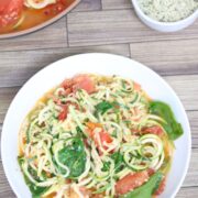 Zucchini noodles and tomato pasta with spinach in a white bowl with more in a pan behind it.