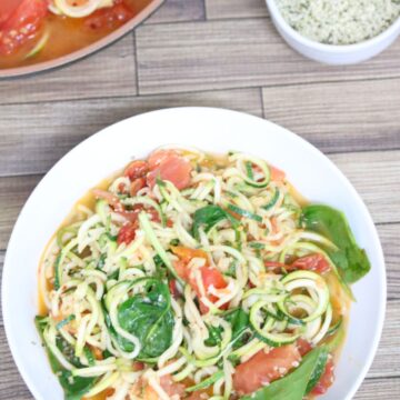 Zucchini noodles and tomato pasta with spinach in a white bowl with more in a pan behind it.