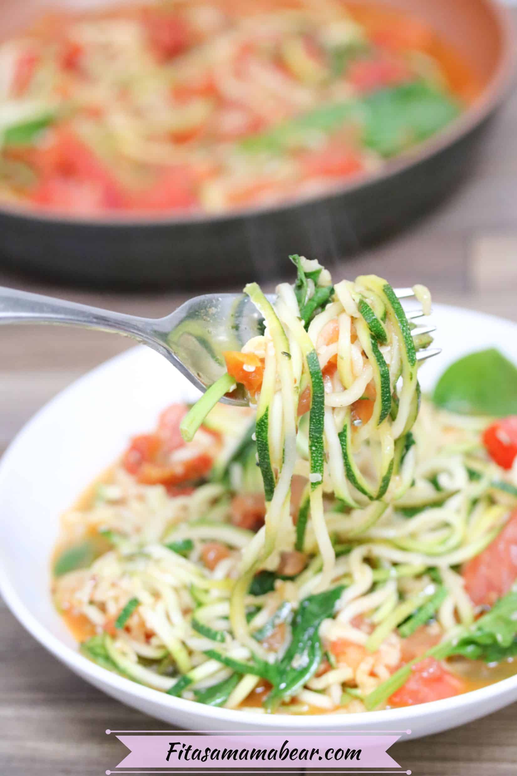 Fork lifting out of a bowl of zucchini noodles with tomatoes and spinach in it.