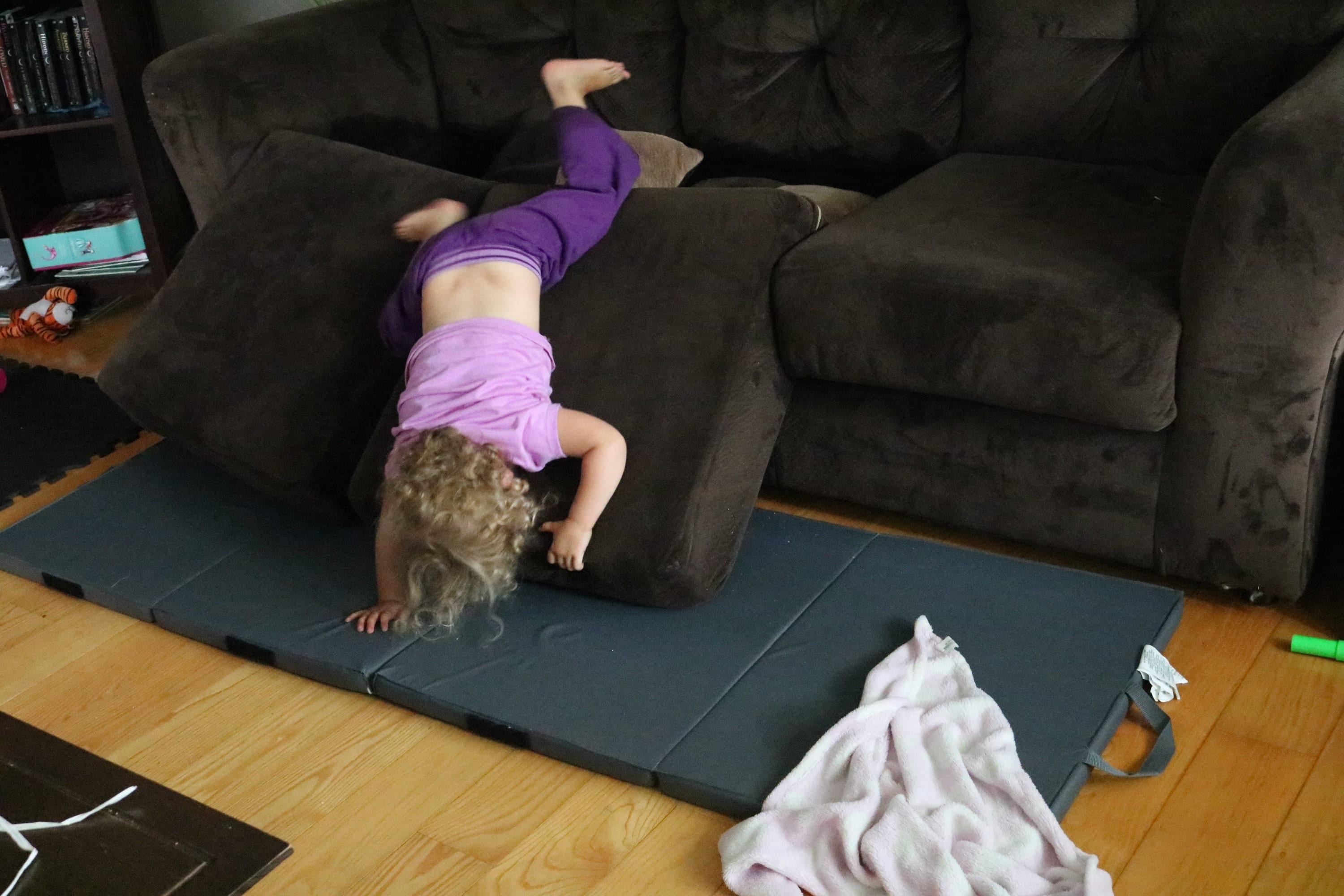Toddler in purple clothes jumping off a brown couch