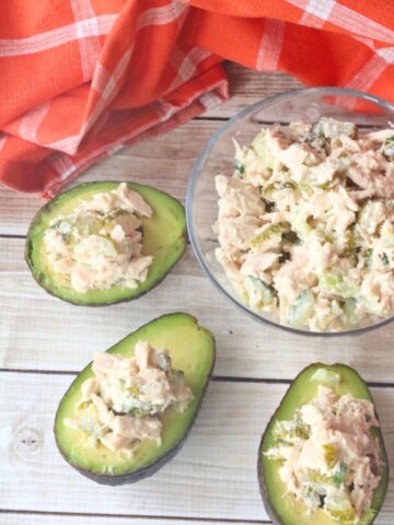 Sliced avocados stuffed with tuna salad around a glass bowl of tuna salad.