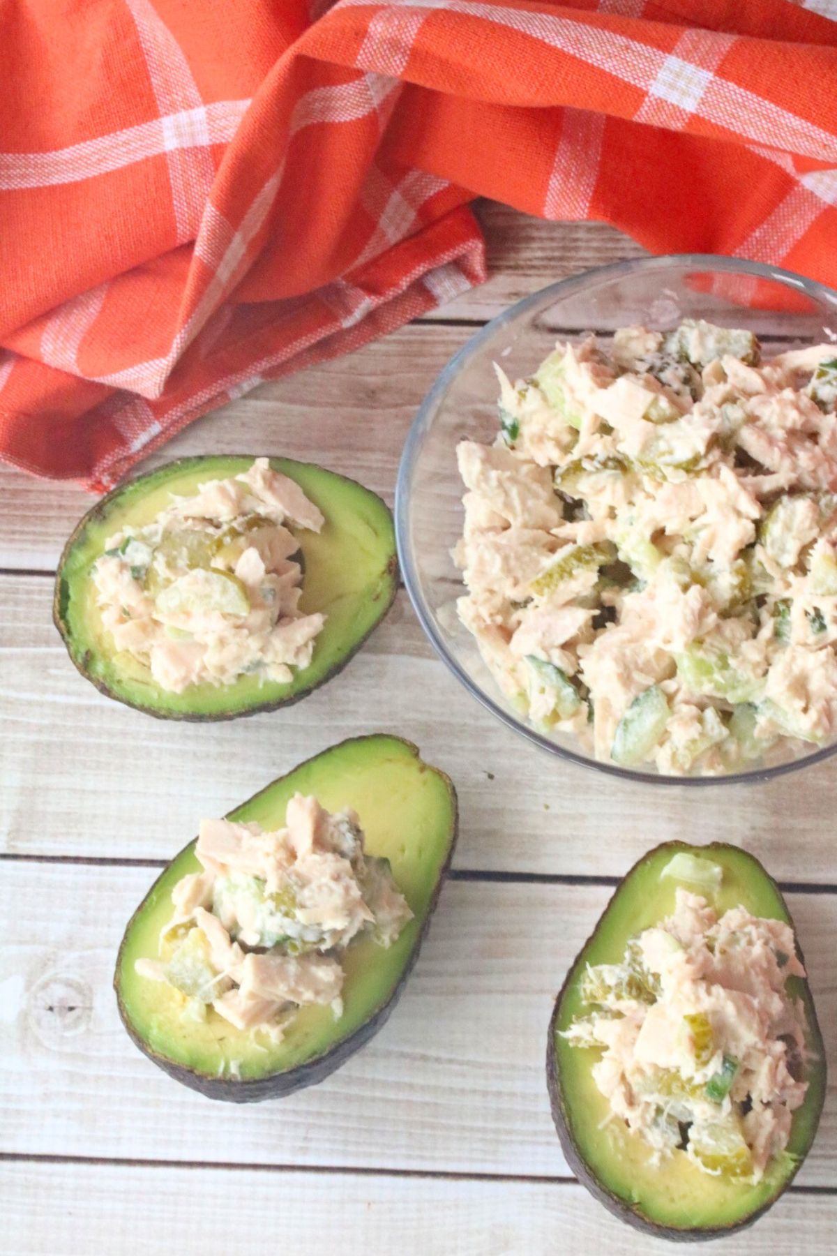 Sliced avocados stuffed with tuna salad around a glass bowl of tuna salad.