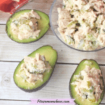 Sliced avocados stuffed with tuna salad around a glass bowl of tuna salad