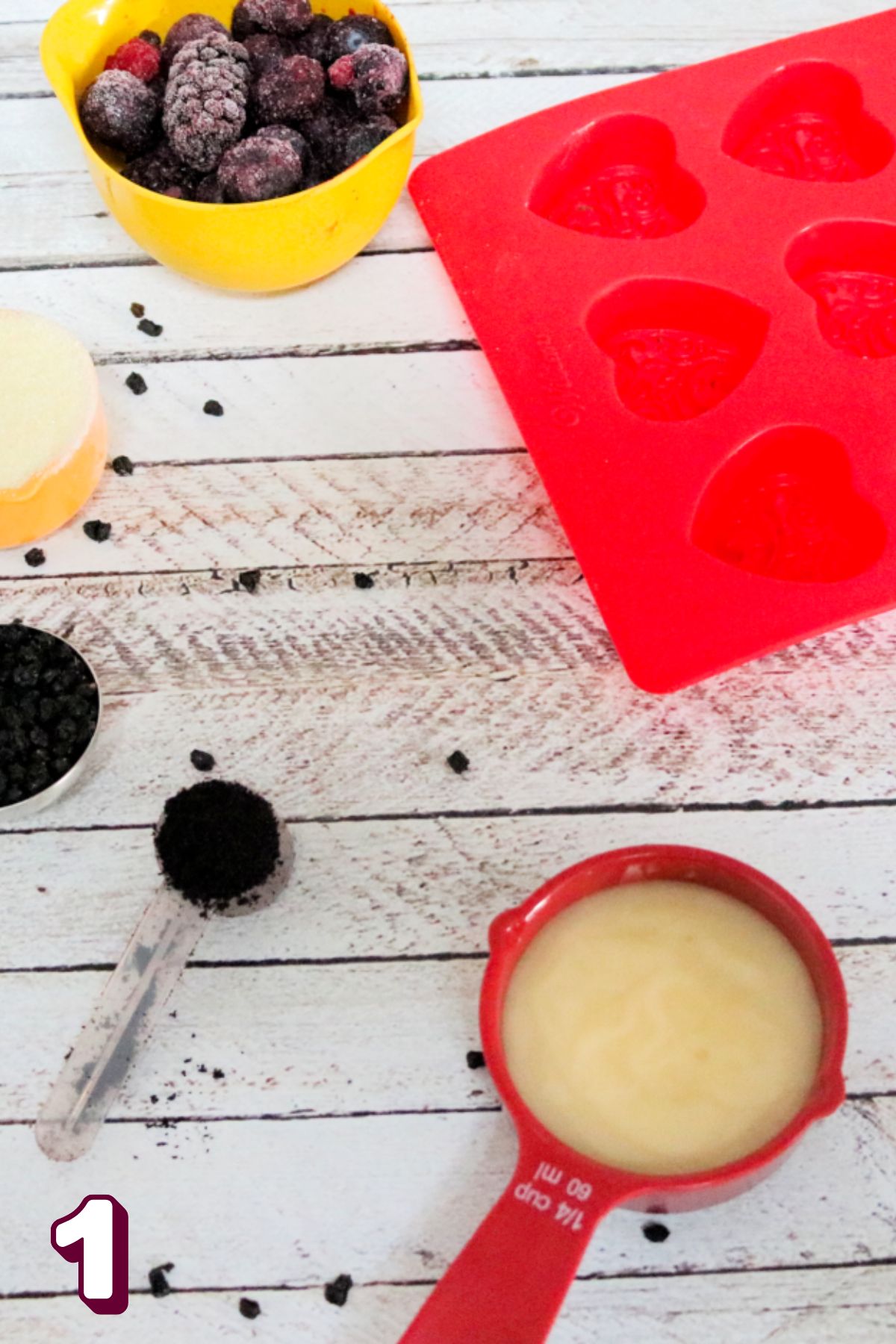 Multiple measuring cups with ingredients beside a red silicone mold.