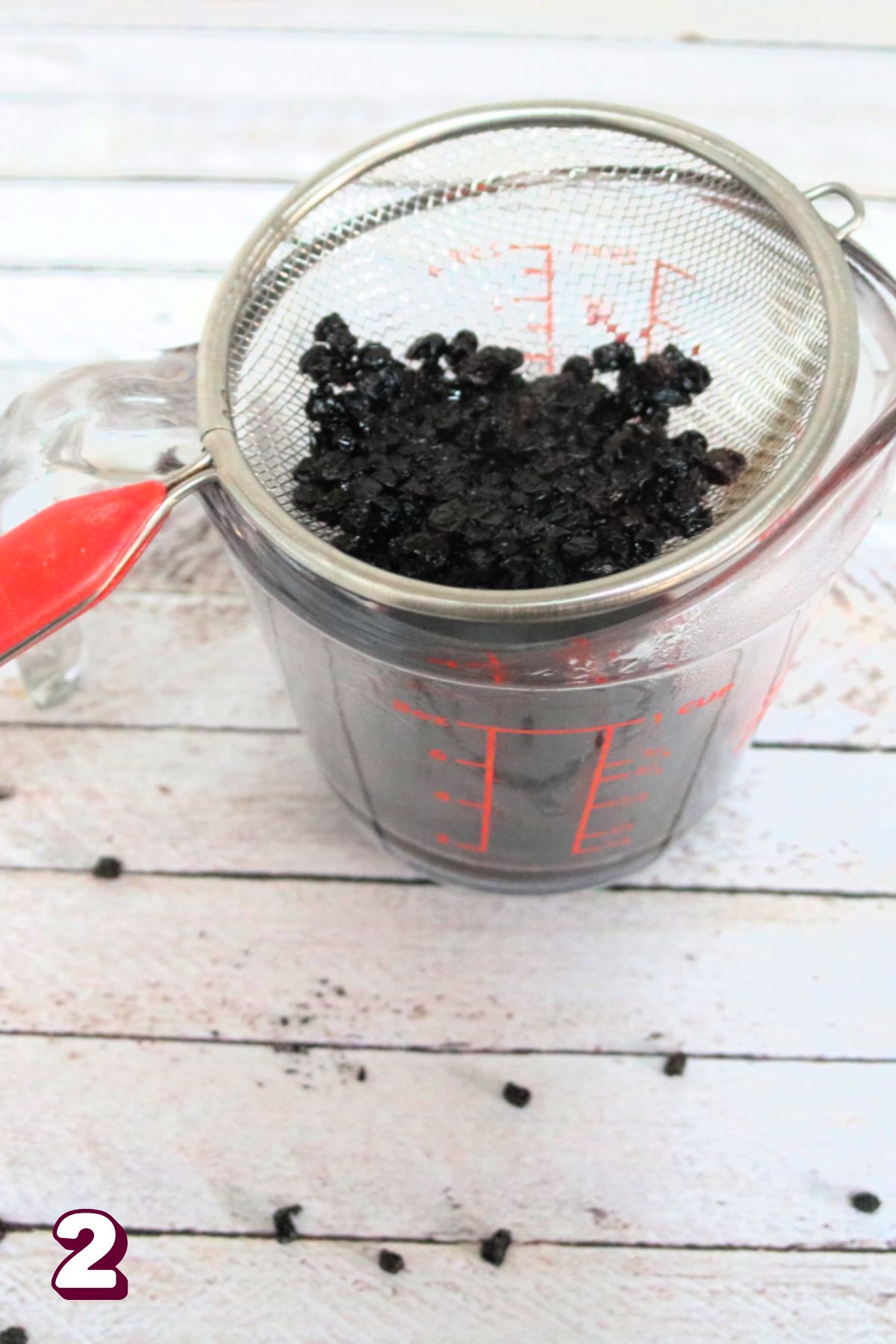 Cooked elderberries being strained by a mesh sieve into a jar.