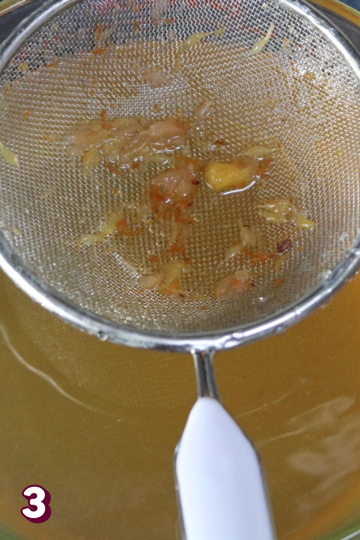 A strainer being held over slow cooker apple cider.