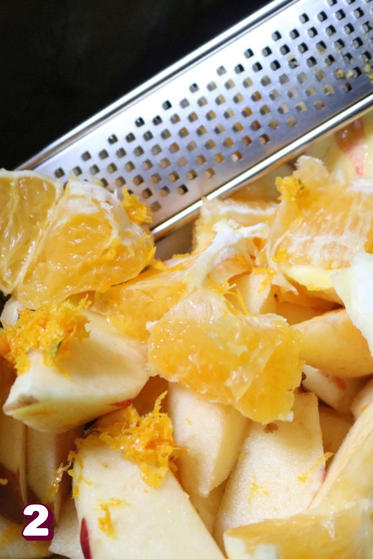 Orange being zested over apples and cut oranges.