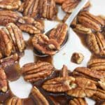 Roasted pecans in maple syrup on a parchment paper lined baking tray with a spoon in the center.