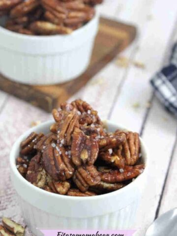 White ramekin with maple candied pecans and a spoon in it with more pecans and a blue linen behind it.