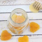 Three honey lemon cough drops around a jar of more cough drops with a honey stick, fresh lemon and a blue linen behind them.