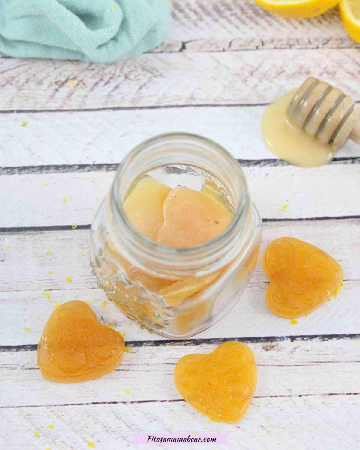 Pin image with text: three honey lemon cough drops around a jar of more cough drops with a honey stick, fresh lemon and a blue linen behind them