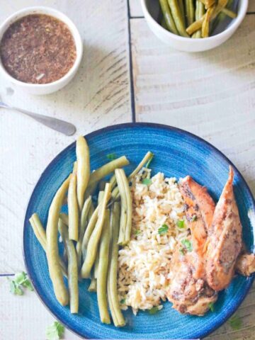 Gluten-free chicken breasts on a blue plate with rice and green beans and sauce in a white ramekin behind it