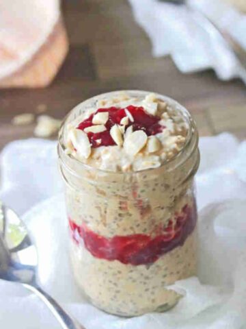 Close up of a mason jar with peanut butter and jelly overnight oats on a white cheese cloth.