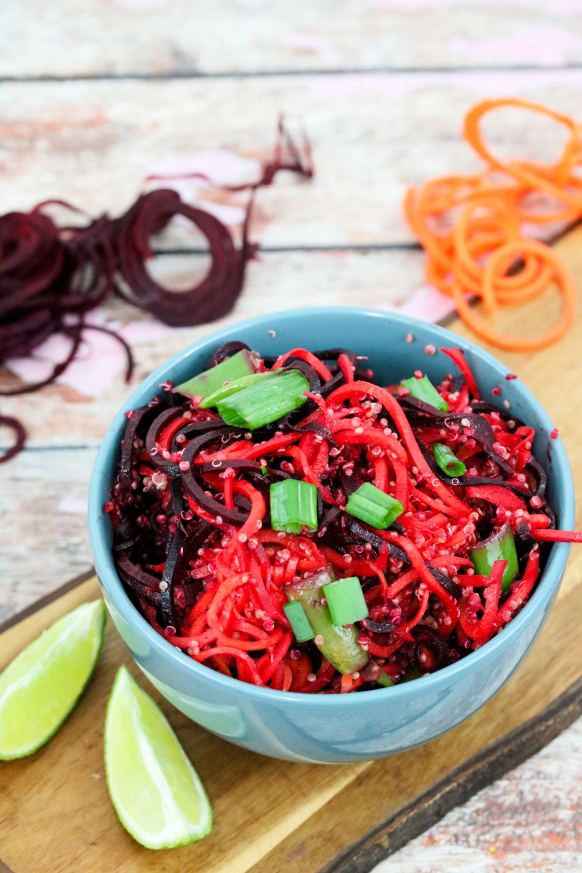 Thai quinoa vegan stir fry in a blue bowl on a cutting board with limes, spiralized carrots and beets around it.
