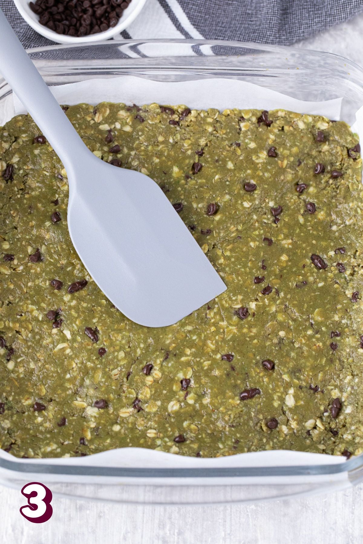 Matcha protein bars topped with chocolate chips pressed into a baking pan wit parchment paper