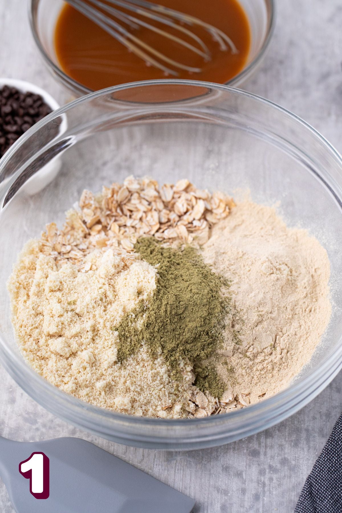 Glass mixing bowl with oats, vegan protein powder, and chia seeds and linens around it.