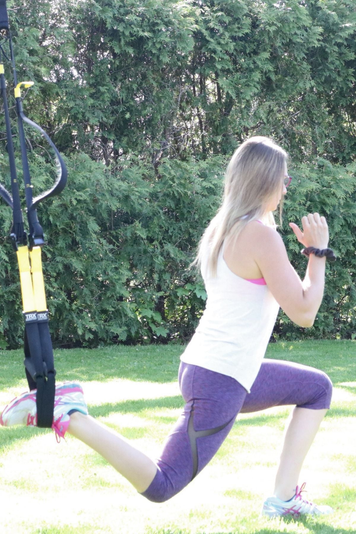 Woman in white shirt and purple pants performing a TRX lunge.