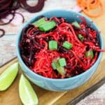thai quinoa vegan stir fry in a blue bowl on a cutting board with limes, spiralized carrots and beets around it