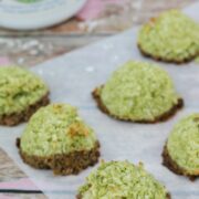 green coconut macaroons dipped in chocolate on parchment paper with a container of energy-boosting matchinga behind them