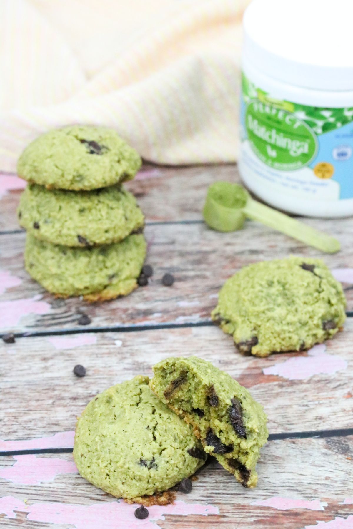 Two green cookies stacked one with a bite out of it and more cookies behind it with a matcha powder tub.